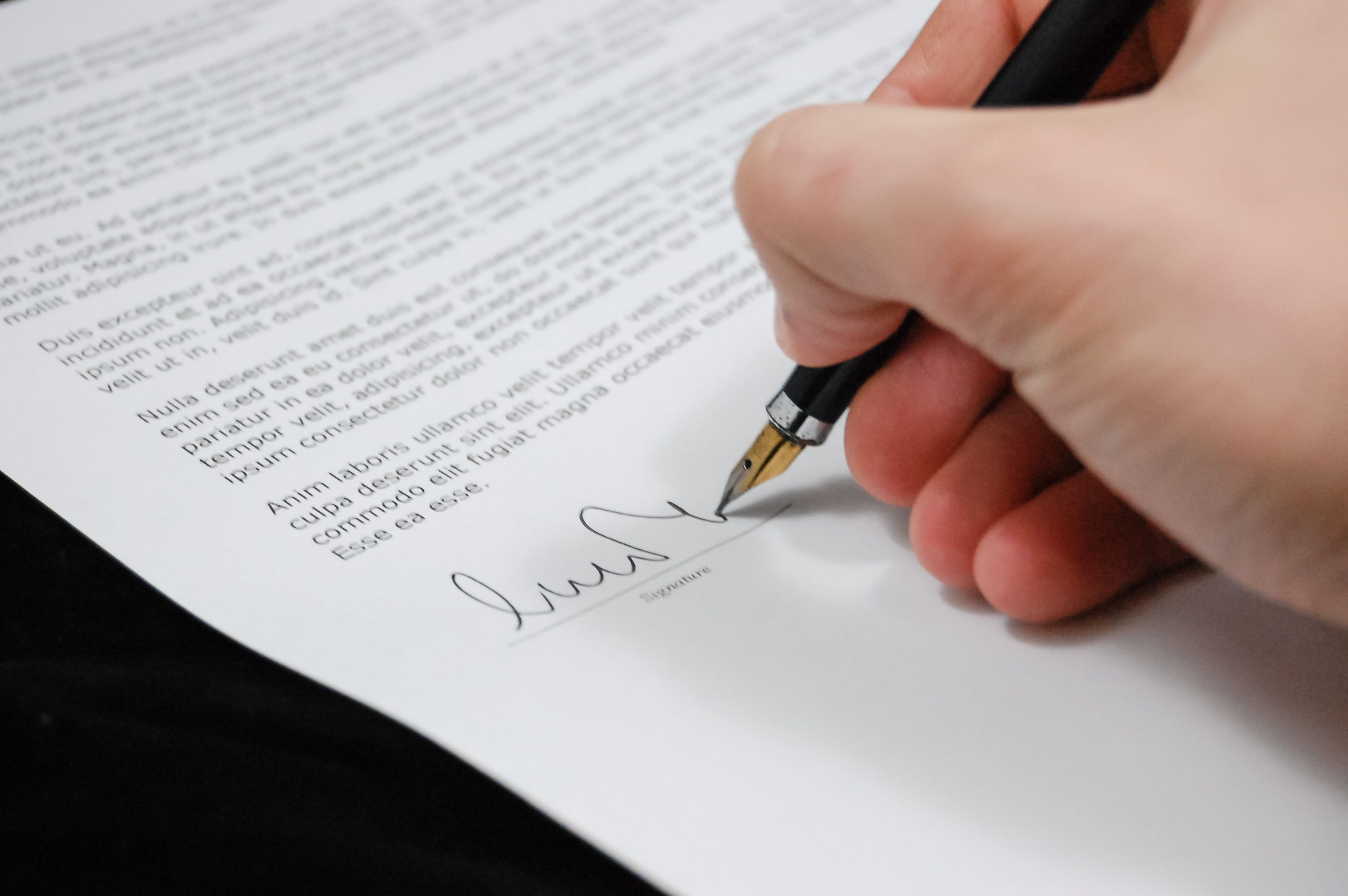 A hand signing a contract with a fountain pen on a signature line.